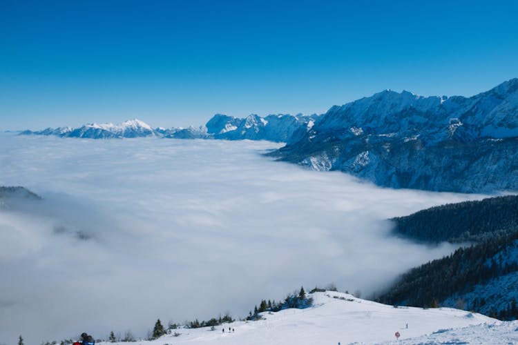 Snowy Mountains With Trees Under Blue Sky On Foggy Day