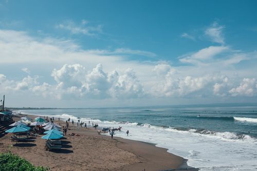 Free Unrecognizable tourists and athletes with surfboards on sandy beach with parasols near foamy sea under blue cloudy sky Stock Photo