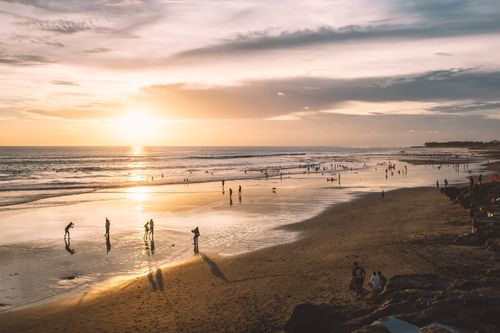 Free Silhouettes of faceless tourists on sandy coast near wavy ocean under cloudy sky at sunset Stock Photo