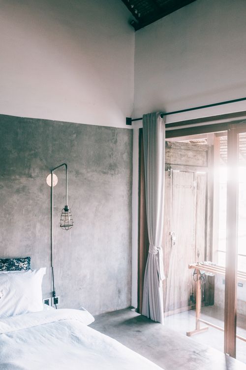 Free Bed with soft blanket and pillow near lantern on concrete wall illuminated by shiny light in house Stock Photo