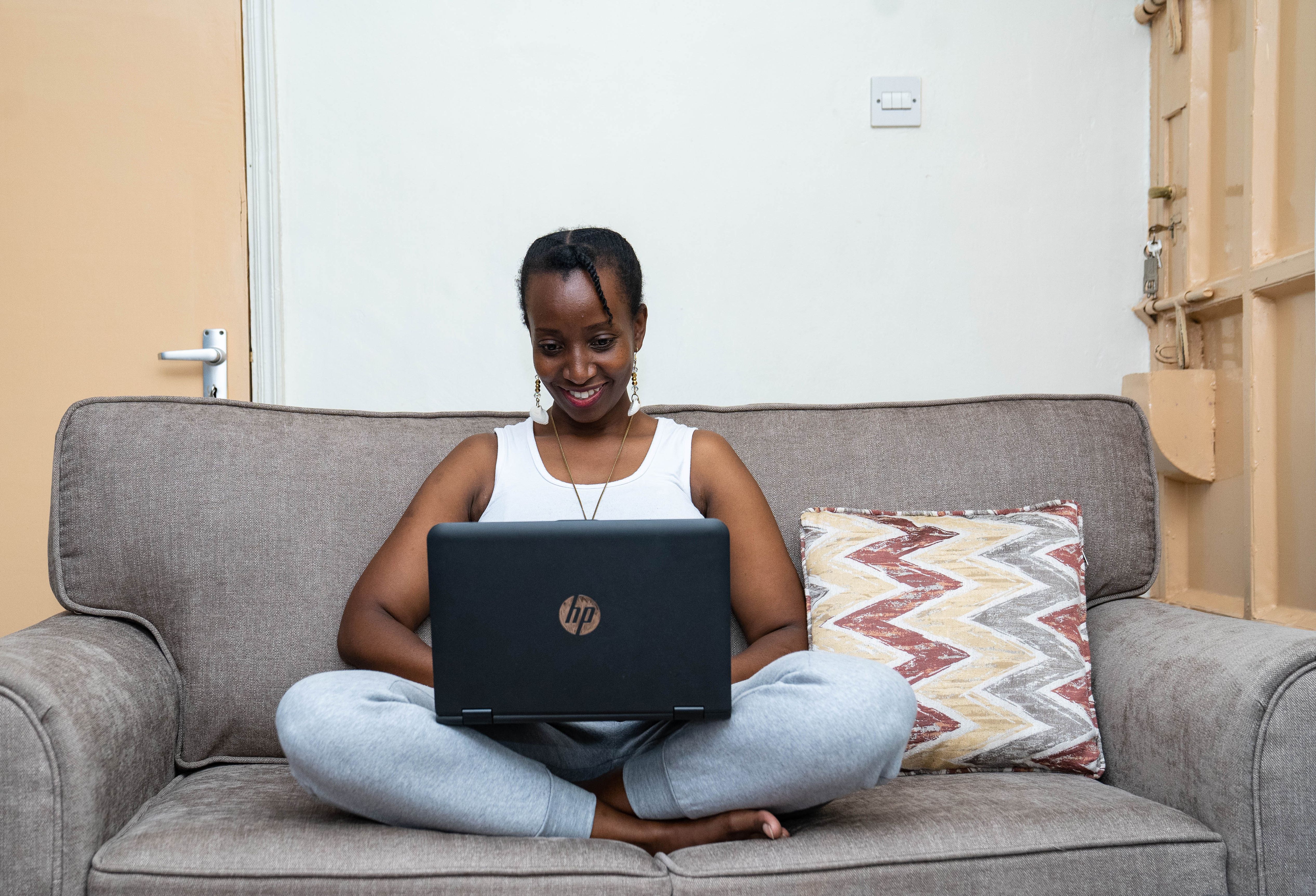 Free African woman using laptop on a couch, embracing remote work style at home. Stock Photo