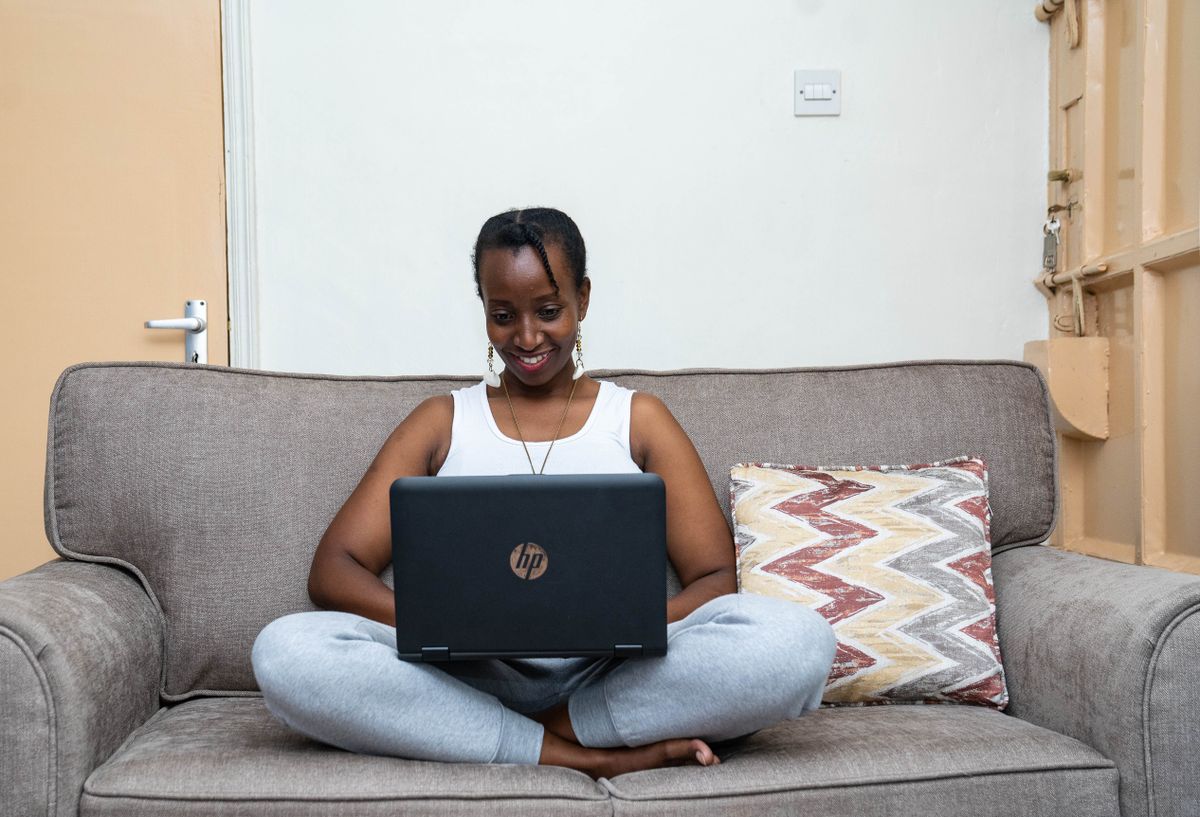 A young woman sits on a sofa at home working on her laptop