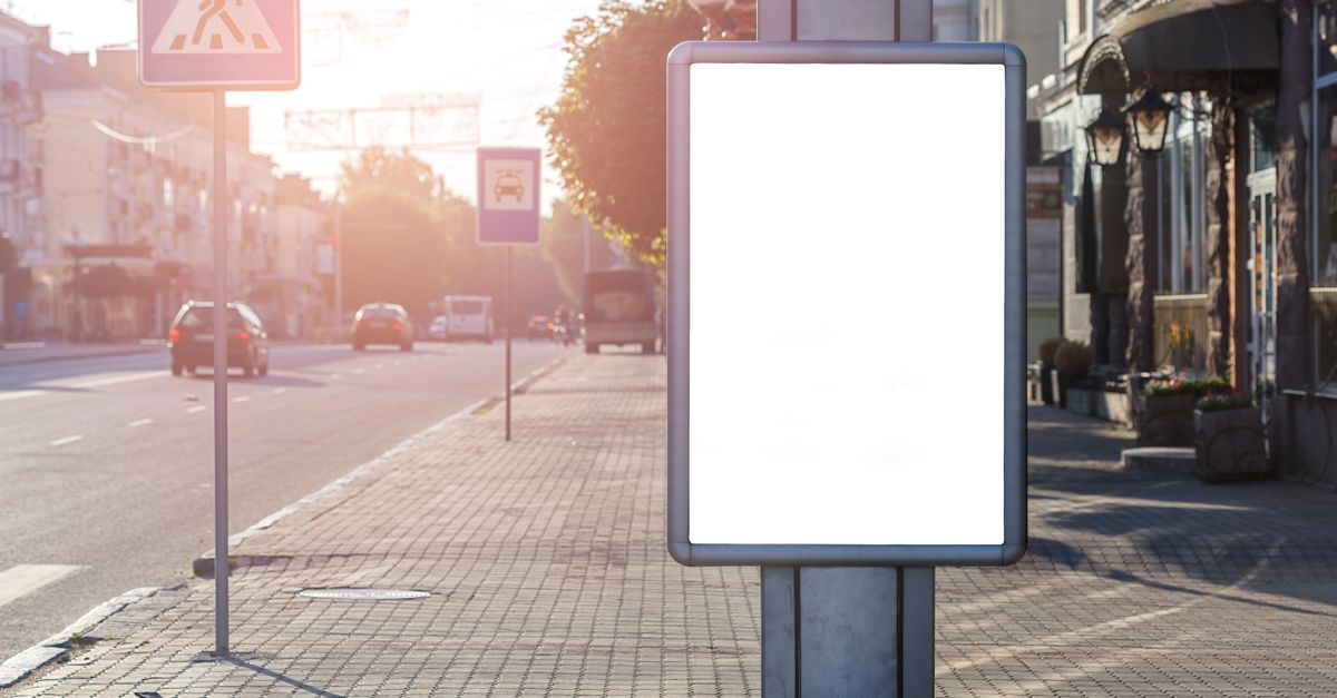 Blank advertisement on tiled walkway with road signs and building in town on sunny day