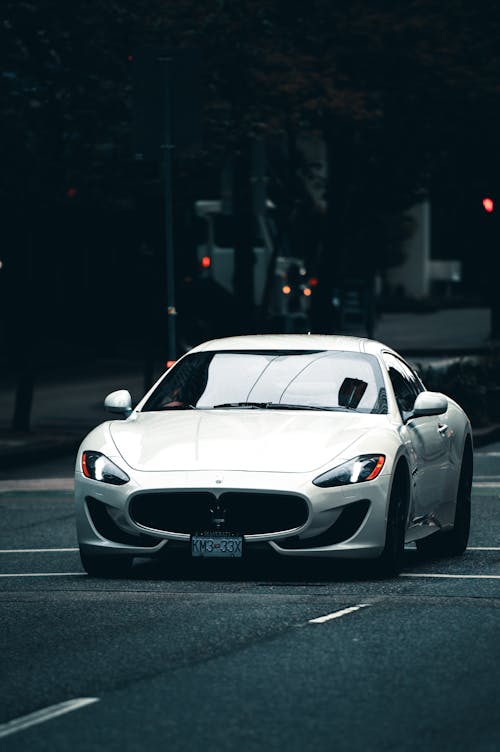 Expensive white luxury sports car with glossy windshield driving on even asphalt automobile road in city in daylight