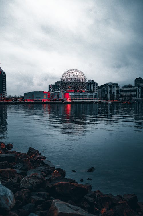 Overcast sky covered with grey clouds over dome of Tellus world of science on shore of reservoir near rocky coast in Vancouver in Canada
