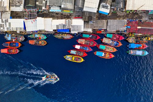 Free Vibrant fishing boats docked at Jakarta's harbor, showcasing a bustling marine scene from above. Stock Photo
