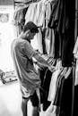 A Grayscale of a Man Looking at Clothes on a Rack