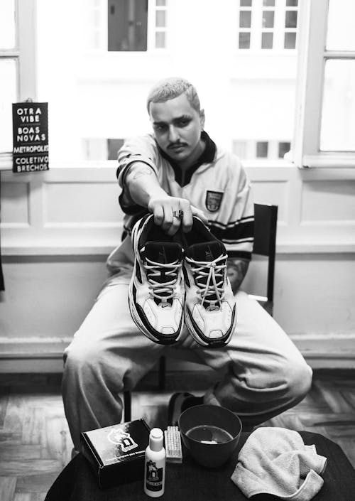 A Grayscale of a Man Holding a Pair of Shoes