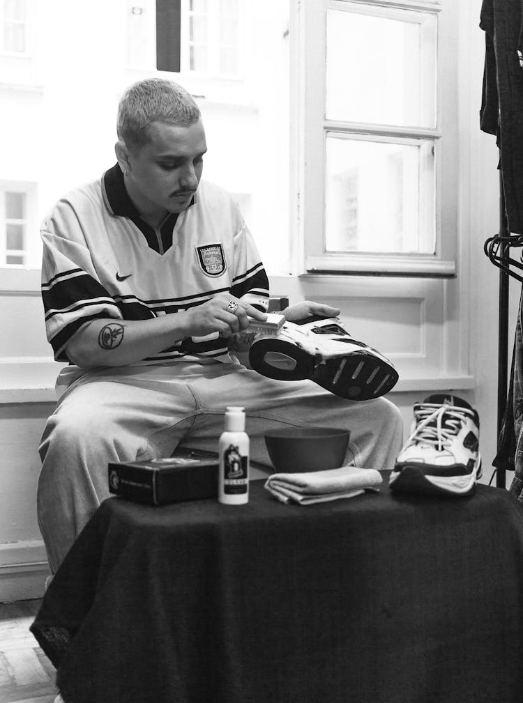 A Grayscale Of A Man Cleaning Shoes