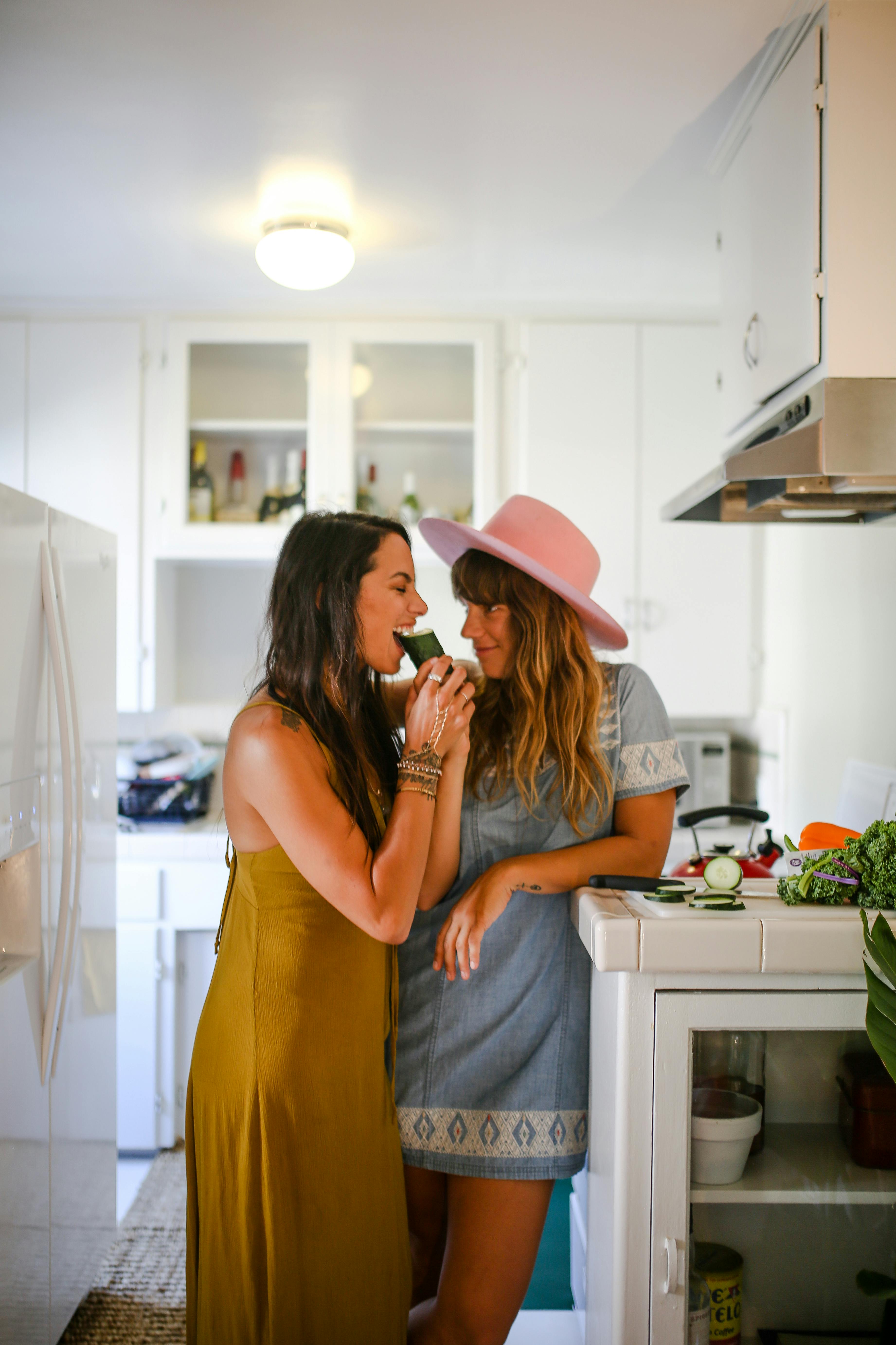 Two women share a lighthearted moment in a kitchen, enjoying a healthy snack together.