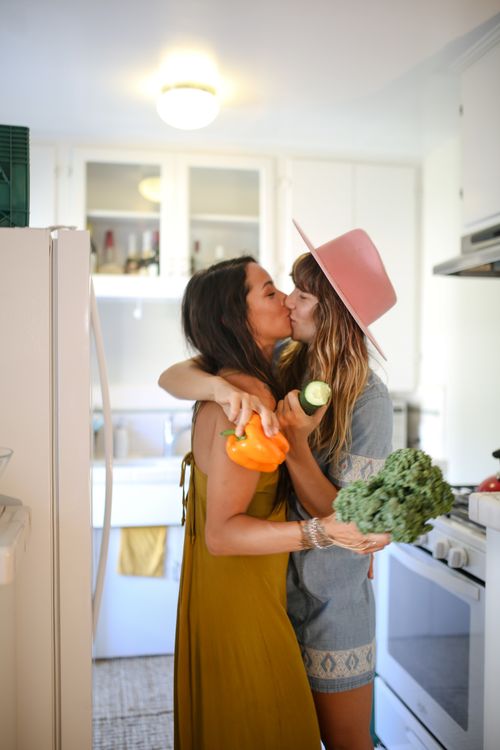 Free A loving couple embraces in a bright kitchen, sharing a kiss while holding fresh vegetables. Stock Photo
