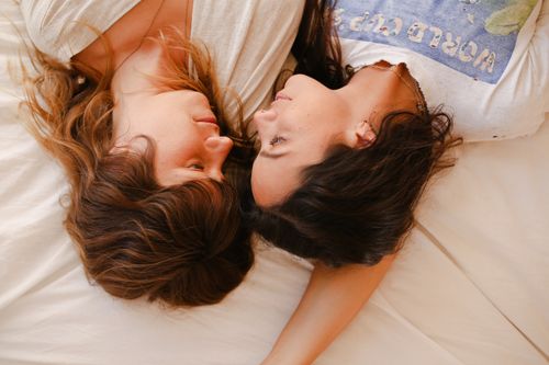 Free A tender moment between two women lying face to face on a bed, showcasing love and intimacy. Stock Photo