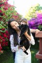 一位长发妇女在户外捧着一只黑猫，周围环绕着充满活力的粉红色花朵