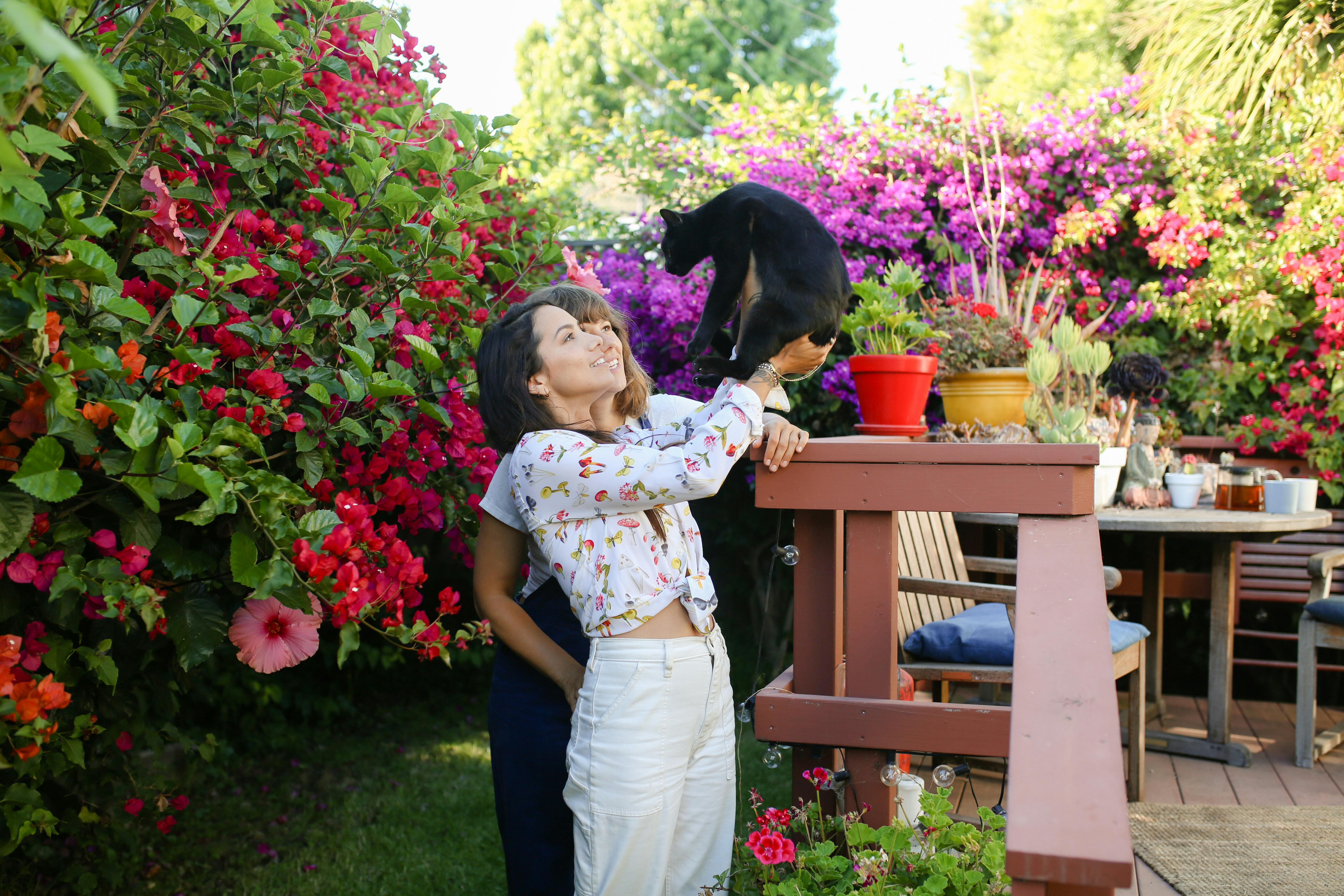 content teenage girls playing with cat in blooming garden