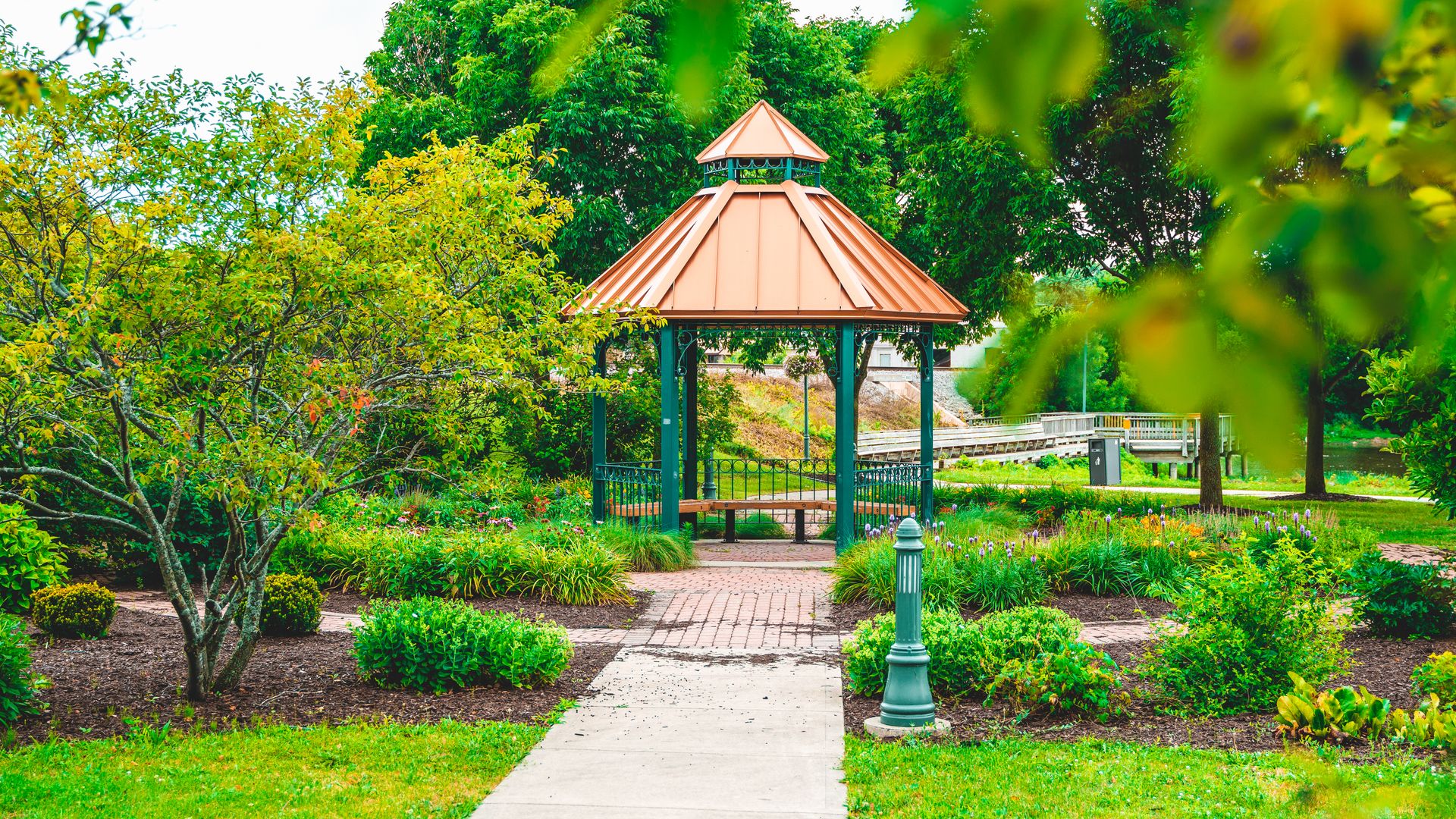 Peaceful gazebo surrounded by vibrant greenery in a lush park setting on a bright day.