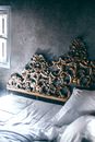 From above of comfortable unmade bed with white sheet and blanket and decorative carved elements on headboard