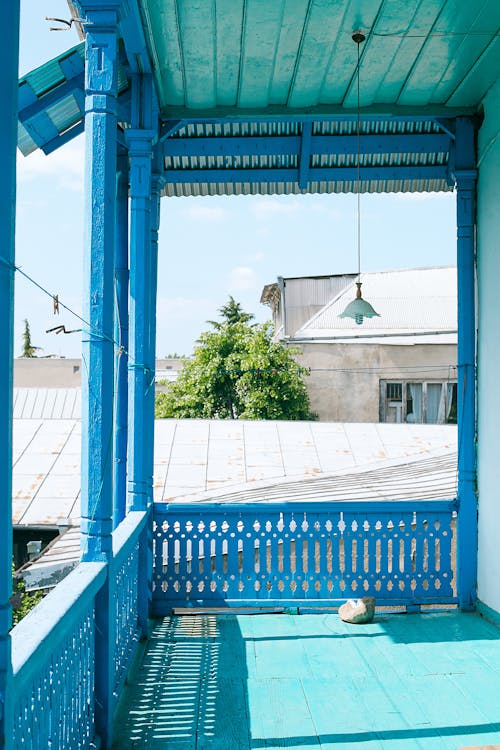 Timber terrace with blue fence of rustic house in sunny settlement with residential buildings