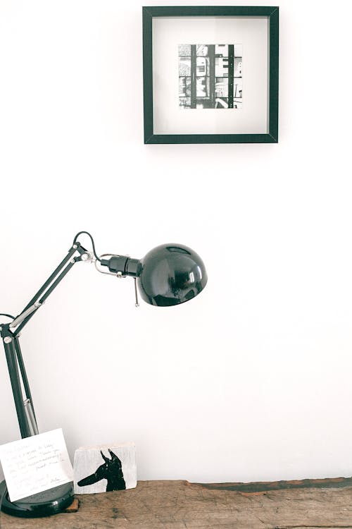 Modern black desk lamp with note placed on wooden table against white wall with picture in light room of cozy apartment