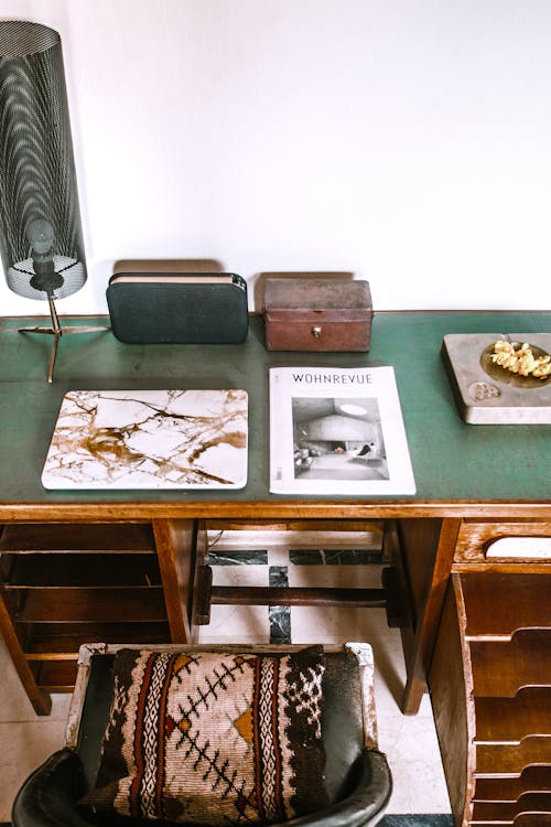 From above of aged desk with lamp near magazine and wooden box against chair with decorative cushion