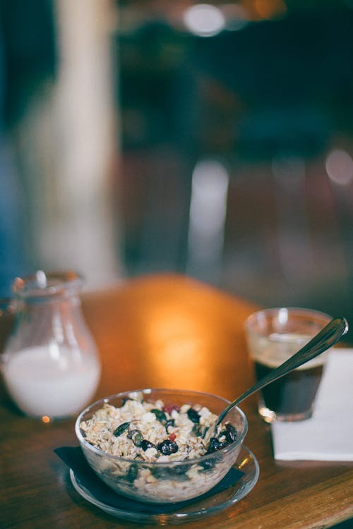 From above of bowl with oatmeal and fresh grapes near glass of black coffee and jug of milk