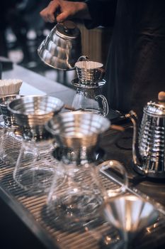 Crop anonymous bartender pouring hot water from shiny coffee maker into dripper in cafe