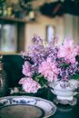 Bright pink peonies in vase near ornamental plate on table