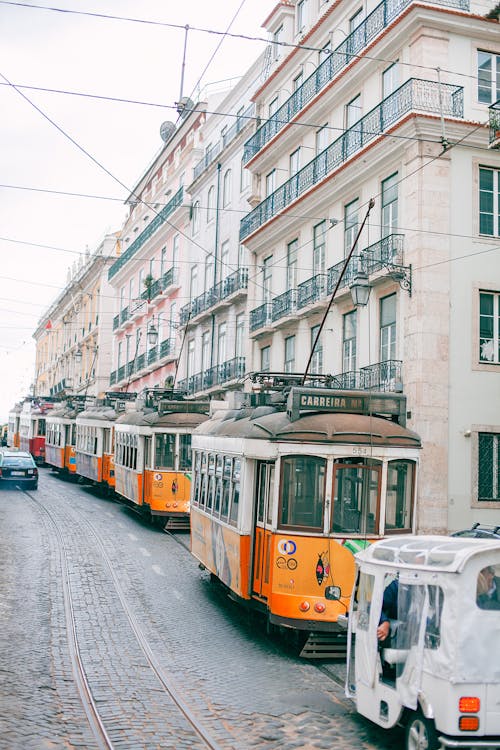 Tramway with bright trams near old multistory stone house facades under white sky in town