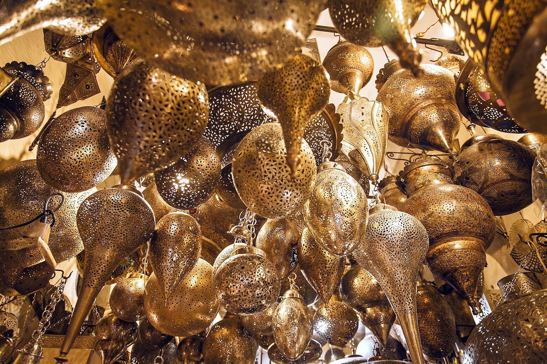 From below of assorted ornamental Moroccan lamps with tiny holes on shiny surface in local market