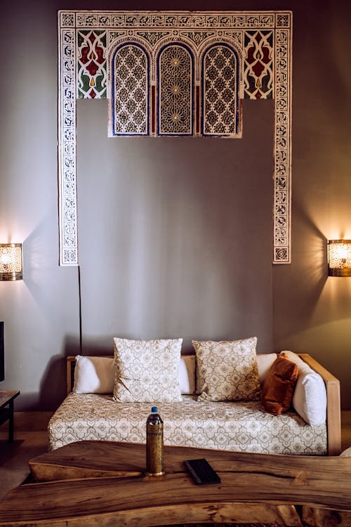 Cozy sofa with decorative cushions near wooden table and shiny lamps on walls in Arabic house