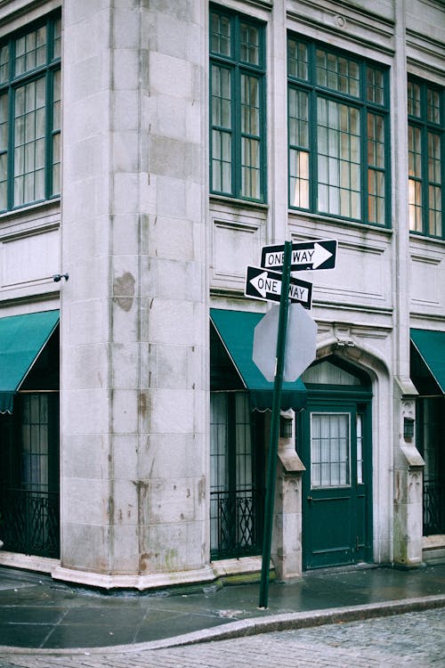 Old building exterior near guide post with One Way inscriptions on sidewalk in city