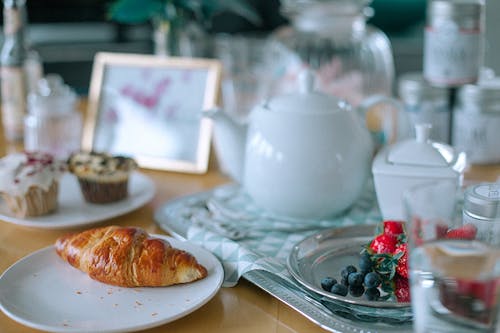 Appetizing croissant and muffins served on table with teapot and berries