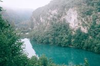 平静的河流中，碧绿的水流在岩石山脉间穿行，山上覆盖着郁郁葱葱的绿树，在雾天的映衬下更显静谧