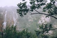 雾天下，绿树成荫的崎岖高山上，瀑布如泡沫般快速奔流，景色壮丽