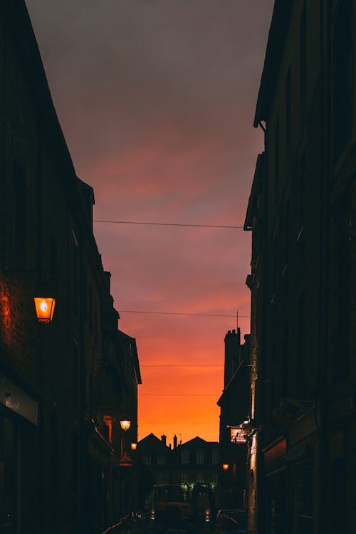 Narrow town street with residential house silhouettes and lanterns beneath majestic dark red sunset sky