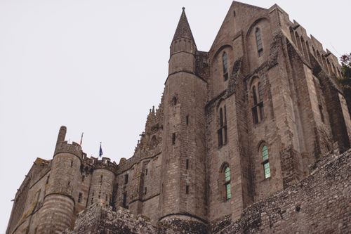 Free From below medieval castle of Mon Saint Michel Abbey with majestic masonry facade in Gothic style against gray sky Stock Photo