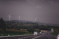 Asphalt highway running through grassy lush valley with modern wind turbine generators under gloomy overcast sky