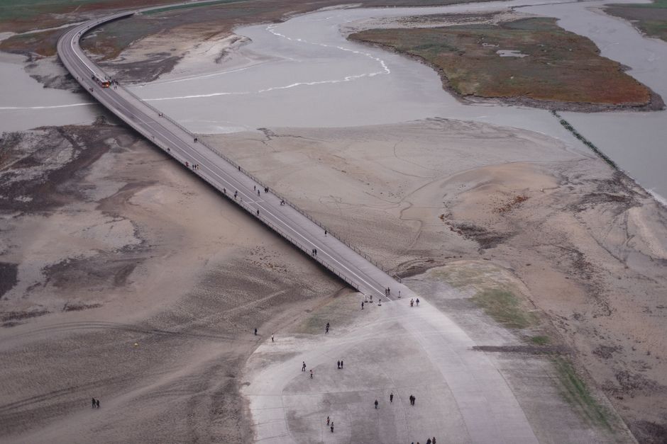 Aerial view of asphalt roadway running over vast flooding river in barren terrain in daylight