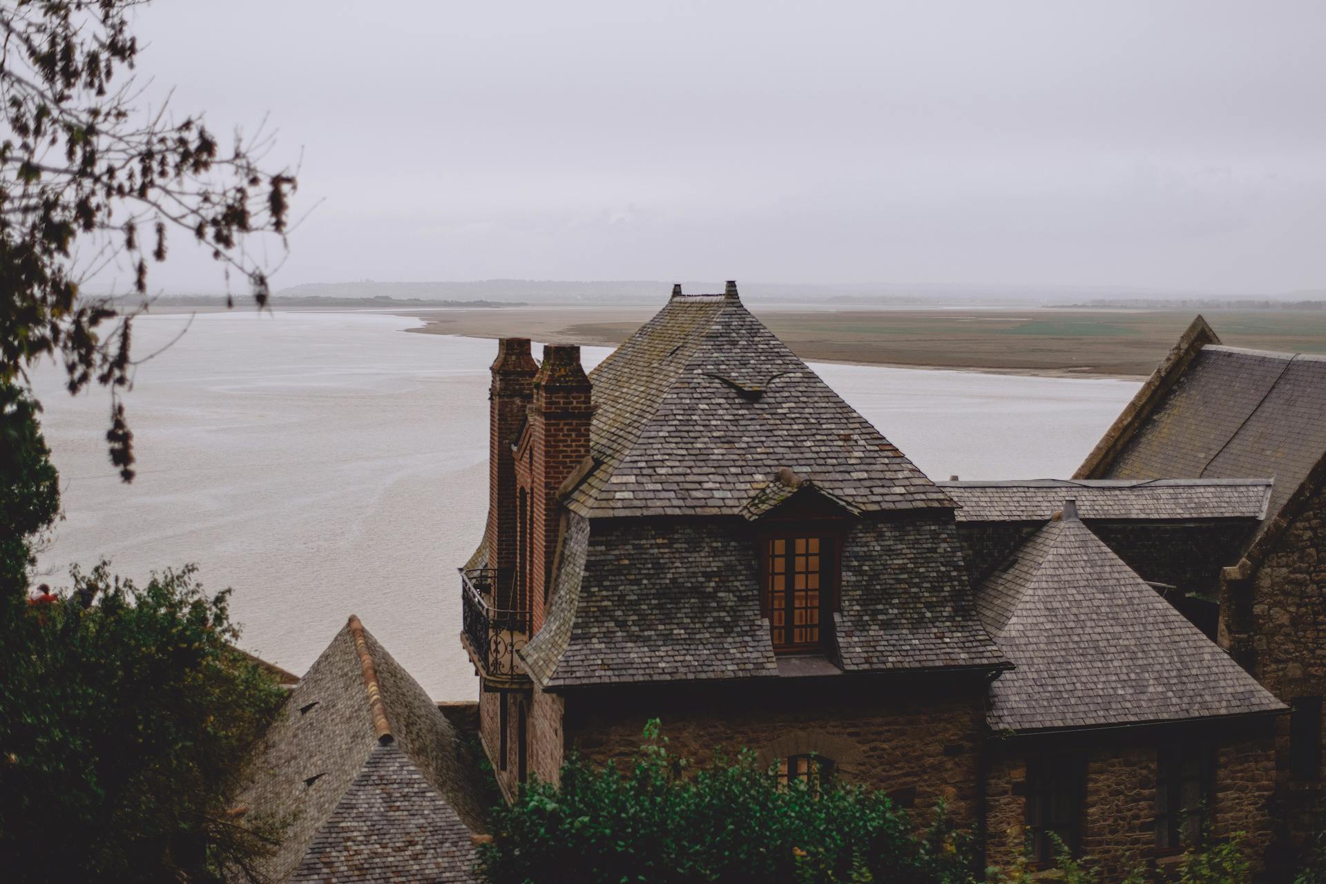 Facade of aged brick castle with tiled roof located on river bank in cloudy countryside