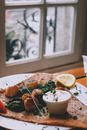 Delicious appetizing seared scallops with spinach served with sour cream and lemon slice on wooden table in seafood restaurant