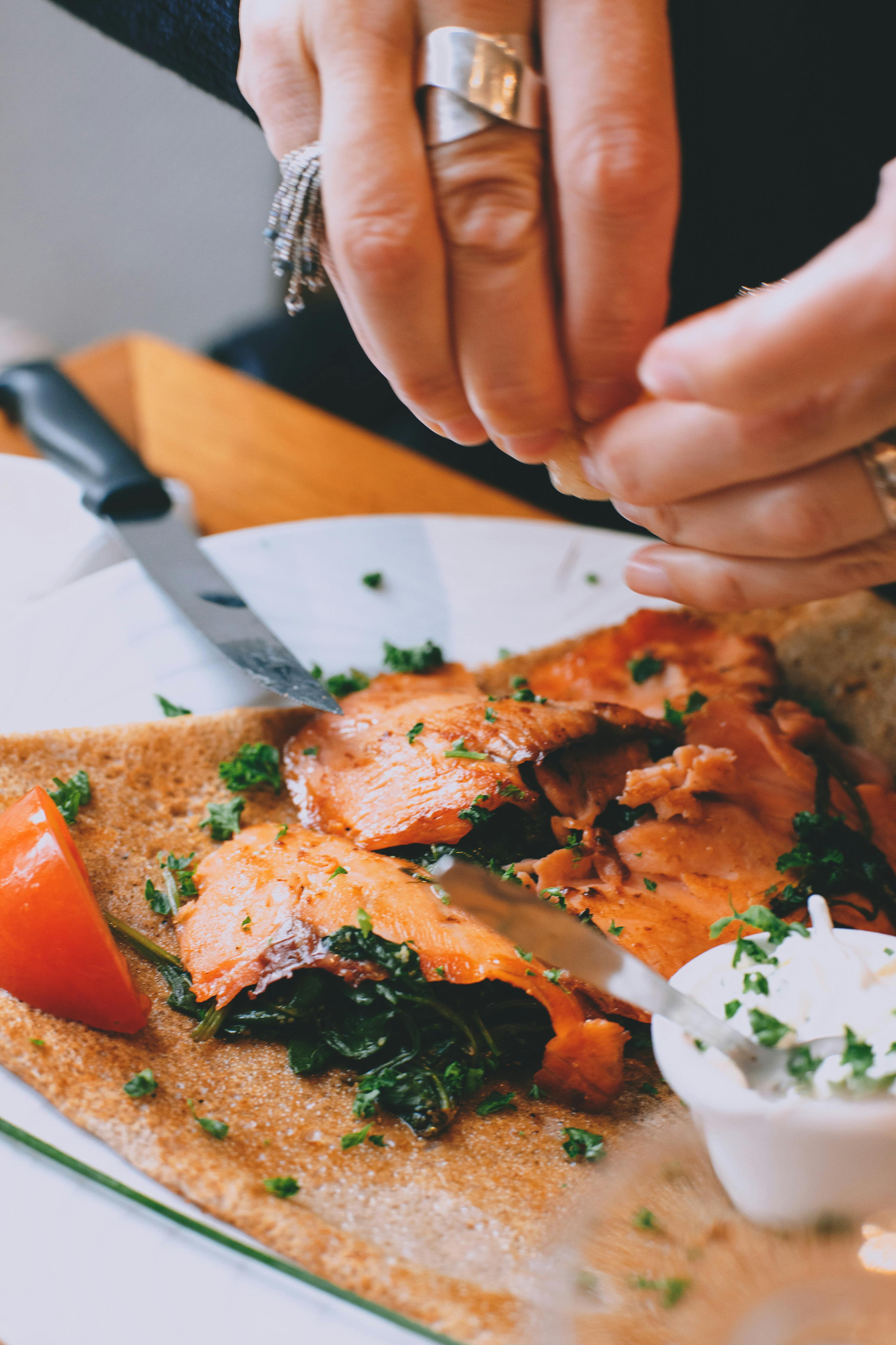 crop faceless woman garnishing salmon steak with herbs