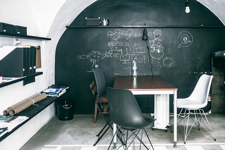 Furniture Near Chalkboard With Illustrations In Empty Workspace