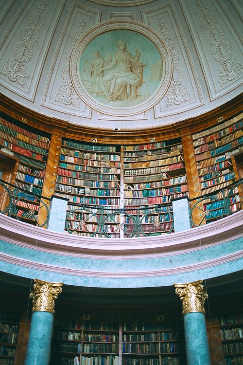 Free Low angle of assorted literature on bookshelves in aged masonry museum with columns and picture on wall Stock Photo