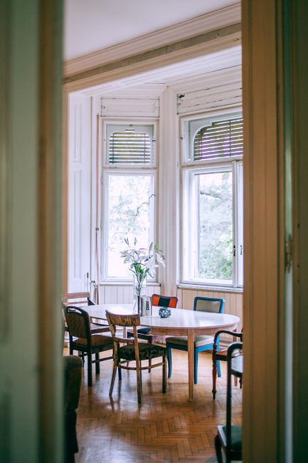 Entrance to comfortable room with flowers in vase on wooden table and various chairs