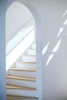 明亮的极简主义室内，白色楼梯带有拱门，自然光投射出阴影