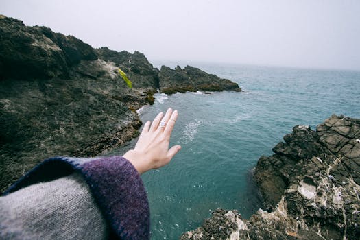 A peaceful coastal scene featuring a hand reaching over turquoise waters and rocky shoreline.