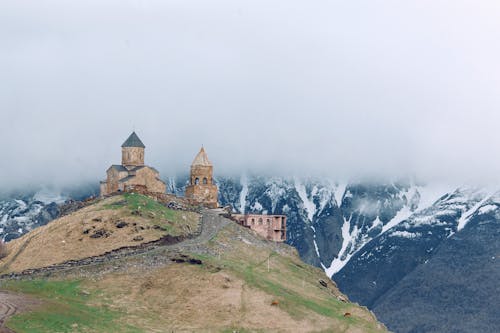 Medieval church on grassy hilltop surrounded by majestic mountains