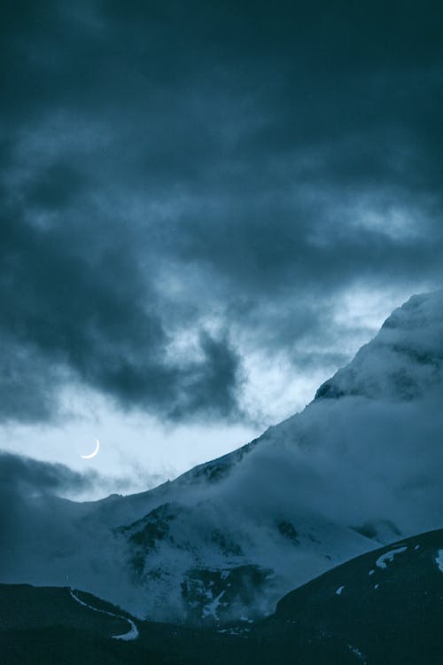 在多雲的夜晚在雪山上空的新月