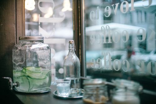 Free Glass jar of cucumber infuse water and bottle of mineral water with glass placed on wooden table with sugar jars located in urban cafeteria Stock Photo