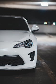 Close-up of a modern white car in an urban parking garage at night, showcasing sleek design.
