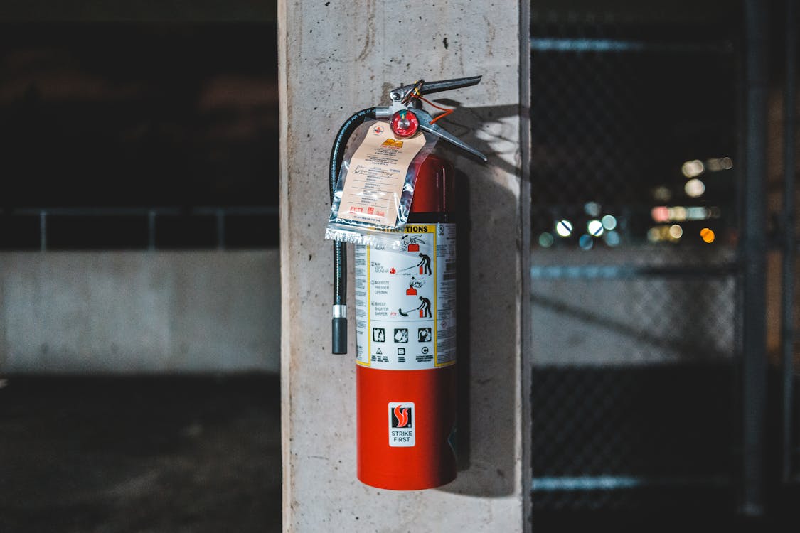 Free Extinguisher with instruction placed on shabby column near chain link on abandoned industrial zone Stock Photo